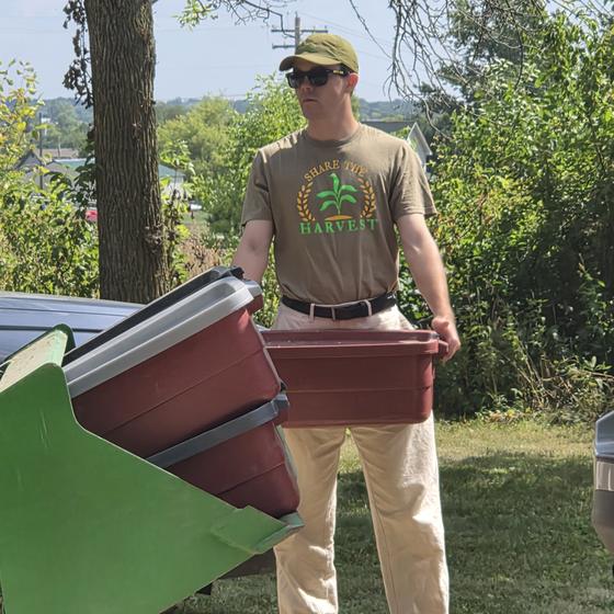 A helper carrying a red bin of collected ingredients to the tractor