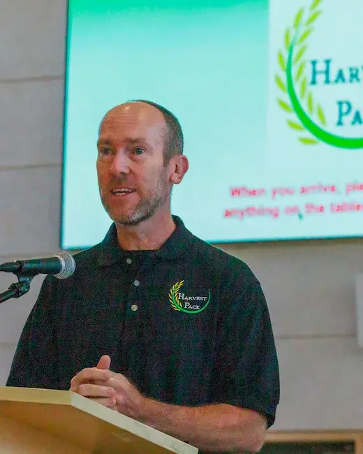 Harvest Pack founder William McNally speaking at the podium during a meal-packing event