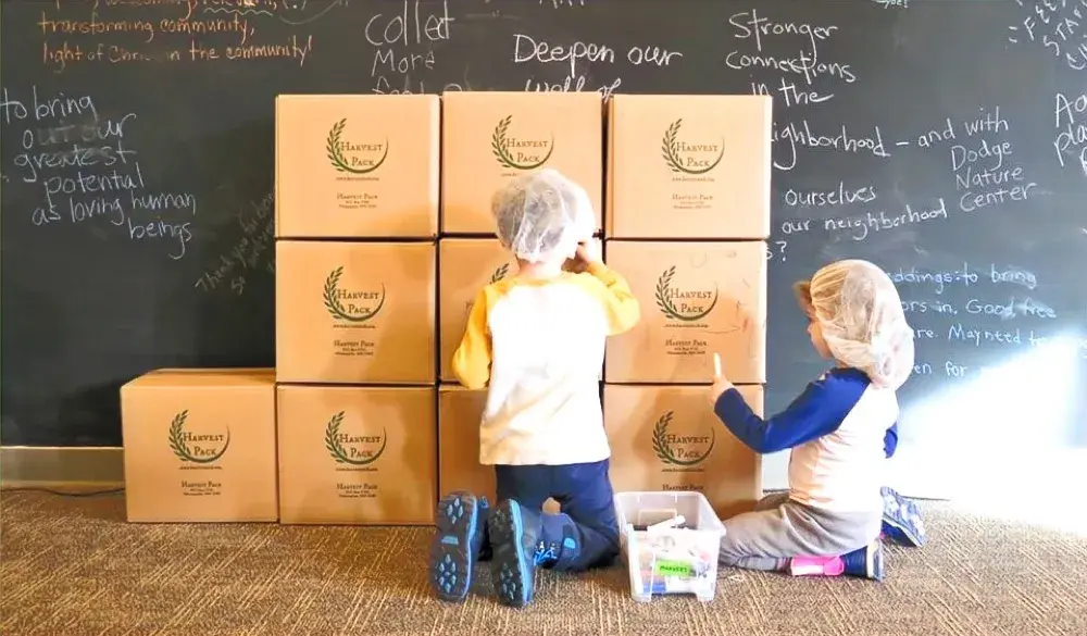 Kids smiling with boxes of healthy meals from a Harvest Pack event
