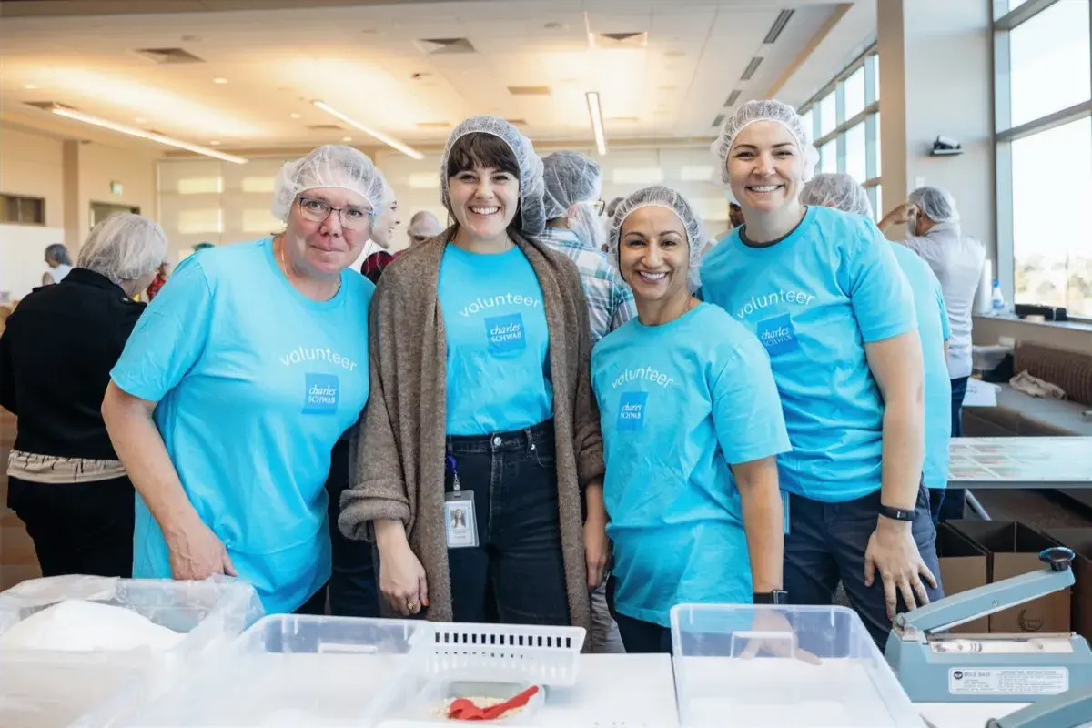 Four volunteers in matching shirts smiling together at a Harvest Pack event