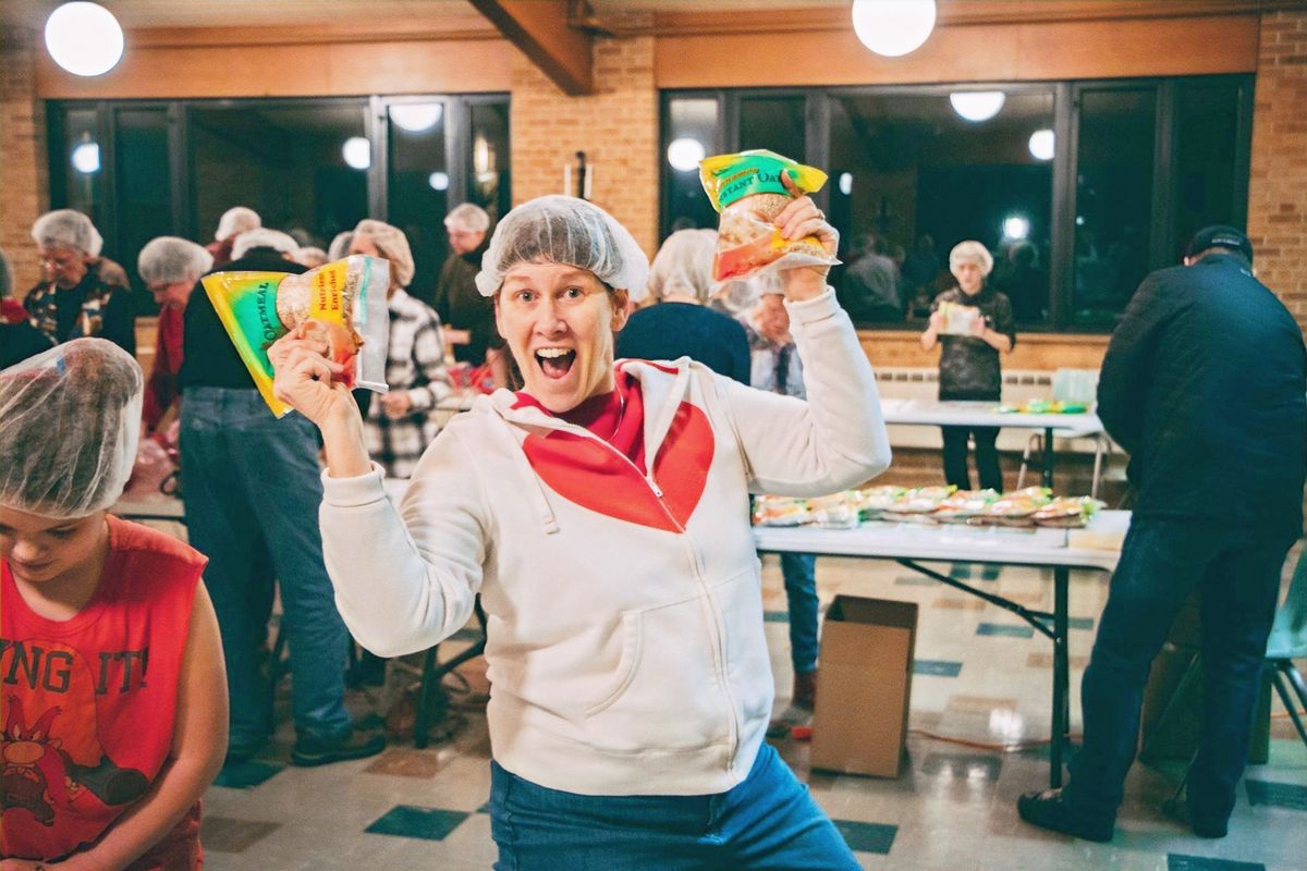 A volunteer in a hairnet cheering with a meal packet in each hand