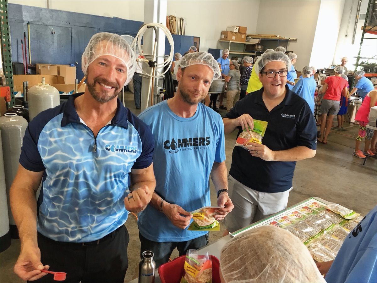 Three volunteers holding meal packets in the Harvest Pack warehouse
