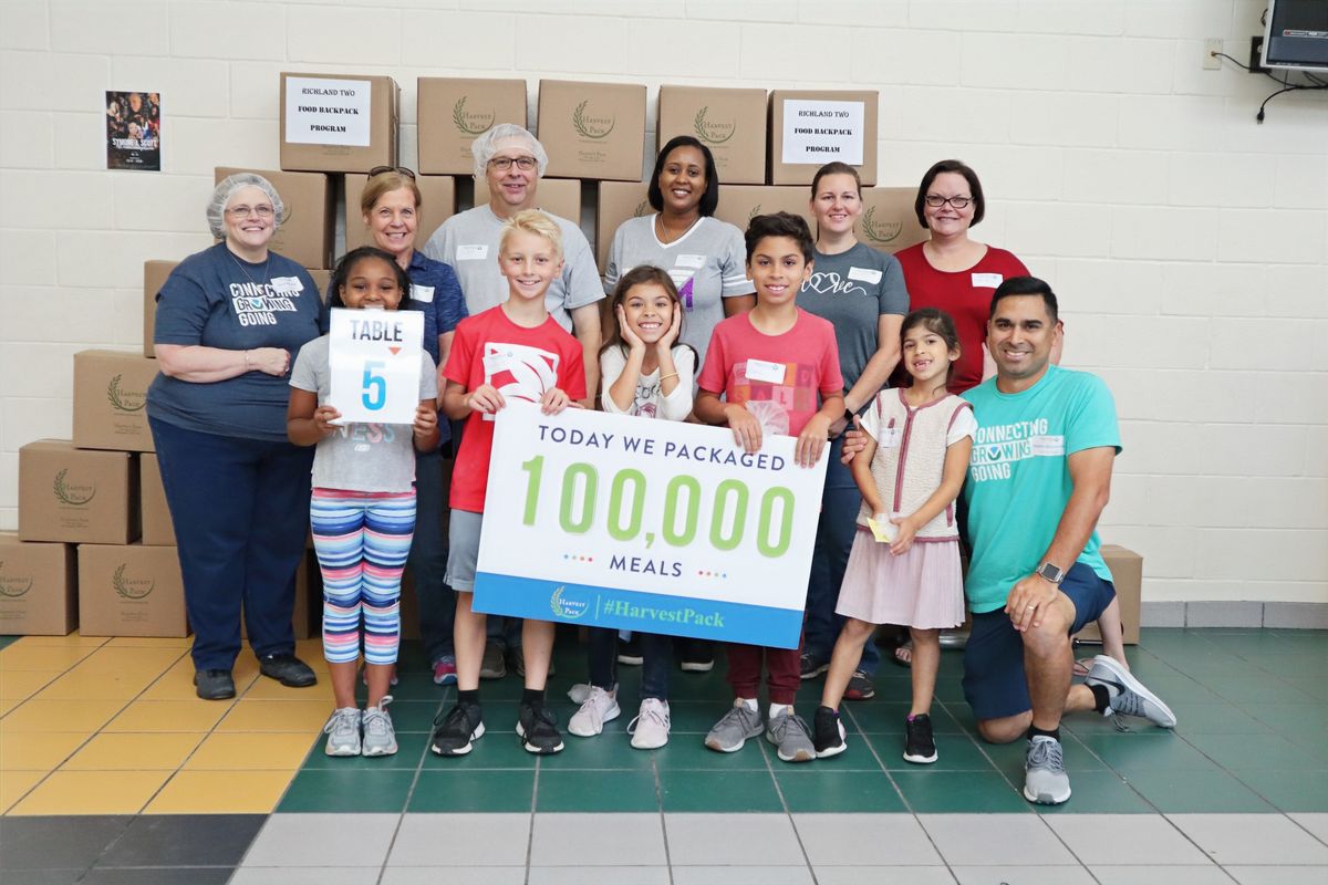Families holding a sign that reads Today we packaged 100,000 meals