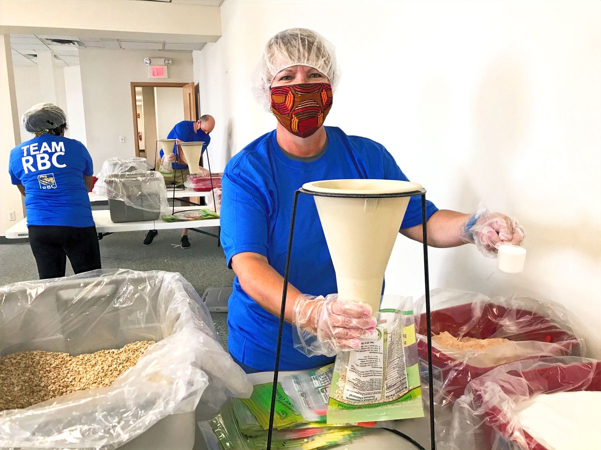 A masked volunteer filling meal bags with a funnel at a 2020 Masked Heroes event