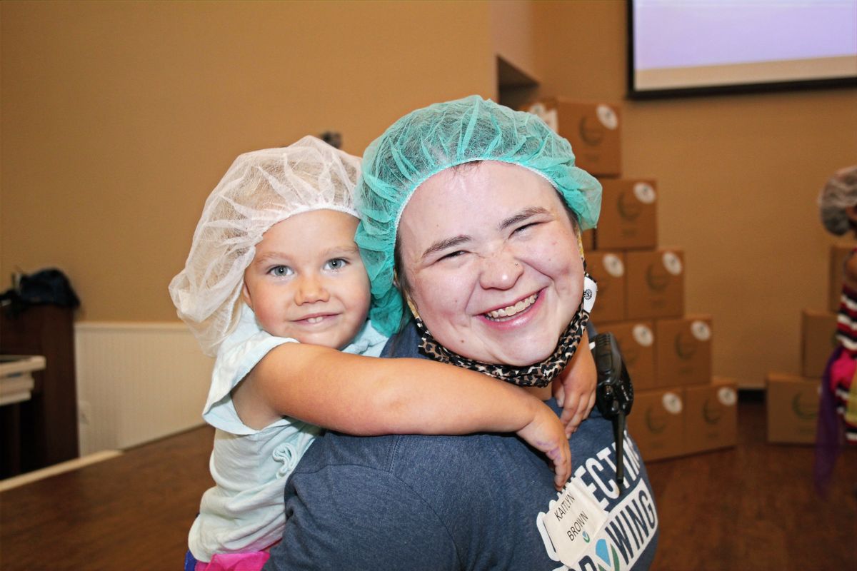 A volunteer in a hairnet hugging a young child at a packing event