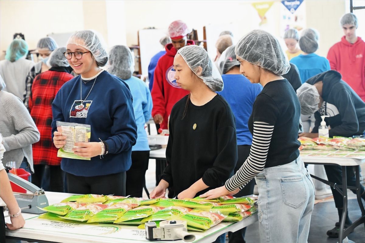 Volunteers in hairnets sealing meal bags on a packing line