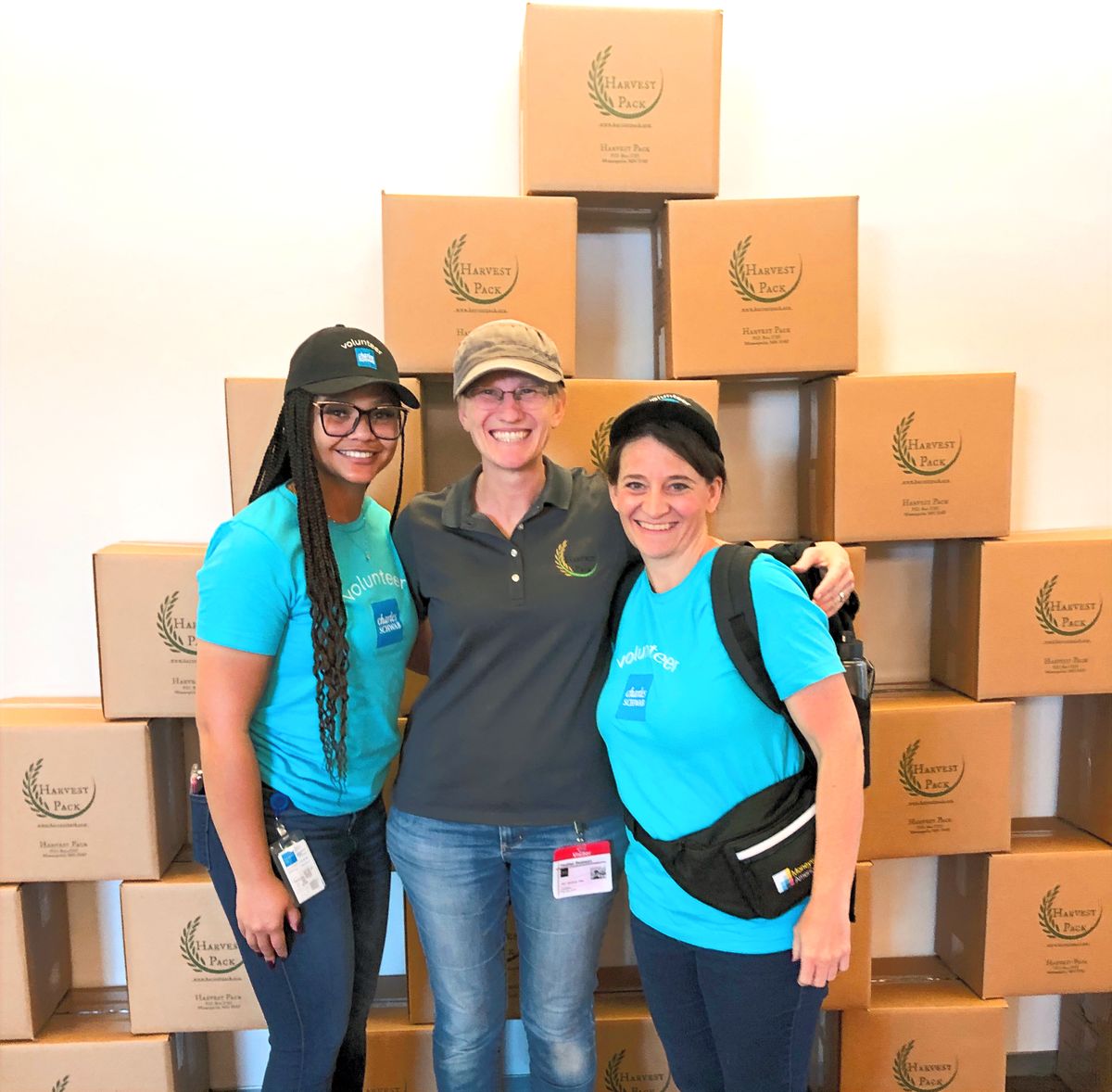 Three Harvest Pack staff members in front of a wall of packed meal boxes