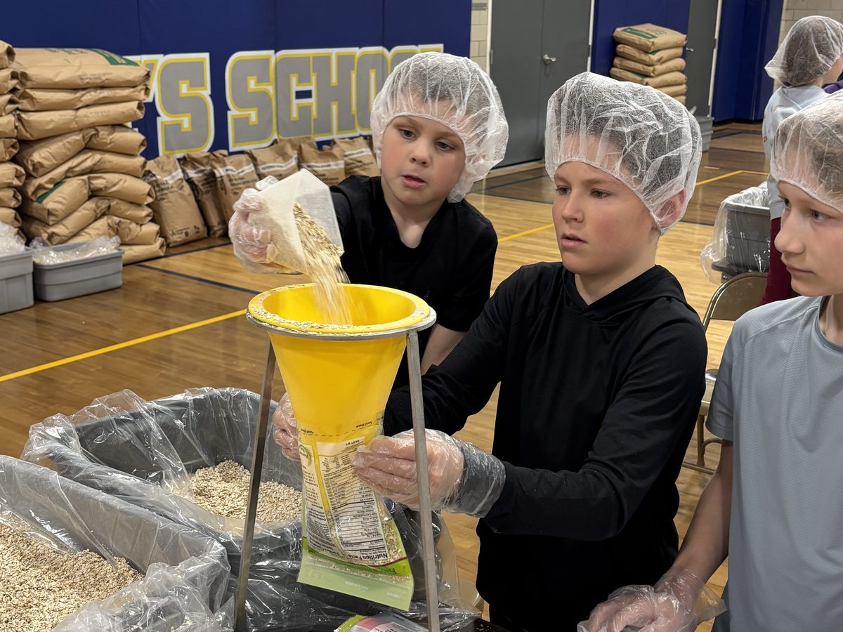 Students in hairnets and gloves filling meal pouches at a school Harvest Pack event